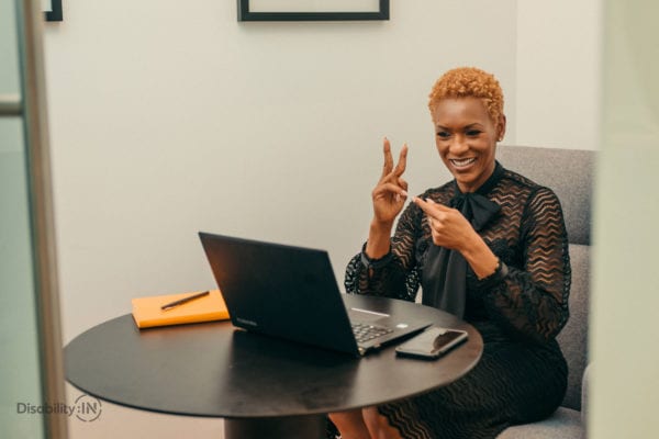 A black woman in a professional setting video conferences while signing into the computer.