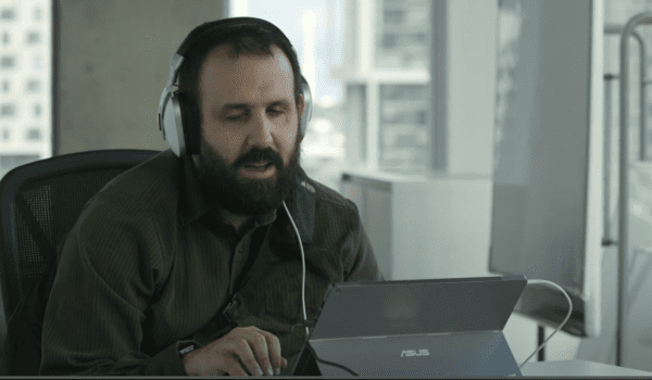 Picture of Sam a white man with a beard wearing headphones and working on a laptop.