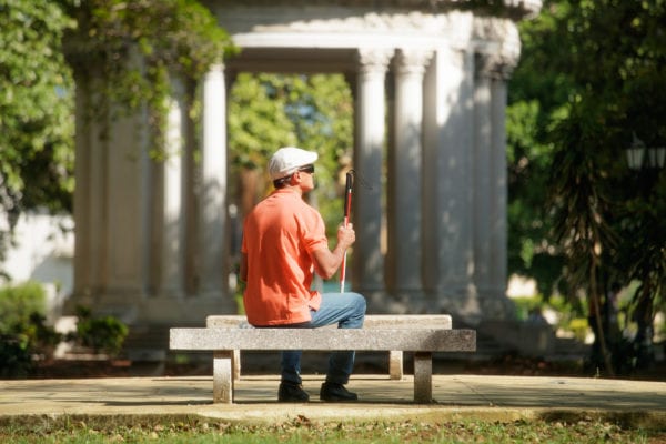Blind man with a cane sitting in a park