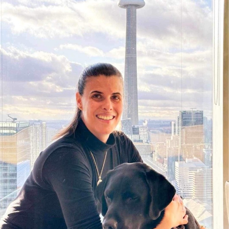 Headshot of Claudia Nigrelli. Claudia is a White woman with brown hair. She is smiling and embracing a black lab dog.