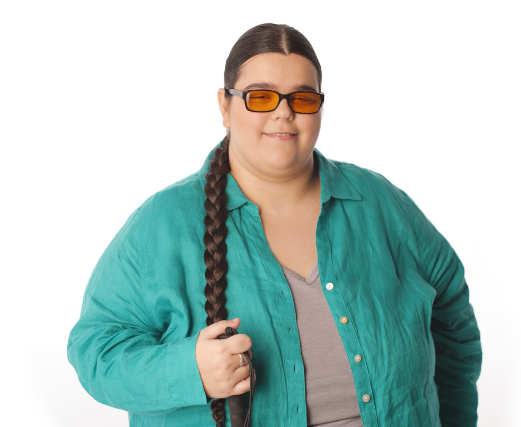 A woman wearing glasses with orange lenses is smiling and holding a cane in her hand. Her hair is in a long braid and she wears a teal shirt.
