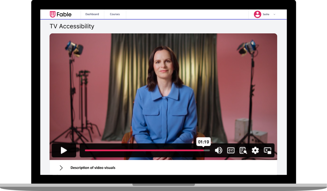 An image of a laptop showing a video player on the screen. The video is of a woman sitting in a studio looking at the camera, smiling.