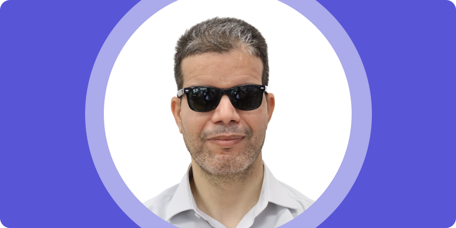 Hamid-A-Banner-mobile Banner image. Portrait of Hamid A., a man with short, dark hair with some gray, wearing black sunglasses and a light-colored collared shirt, set inside a purple circular frame.