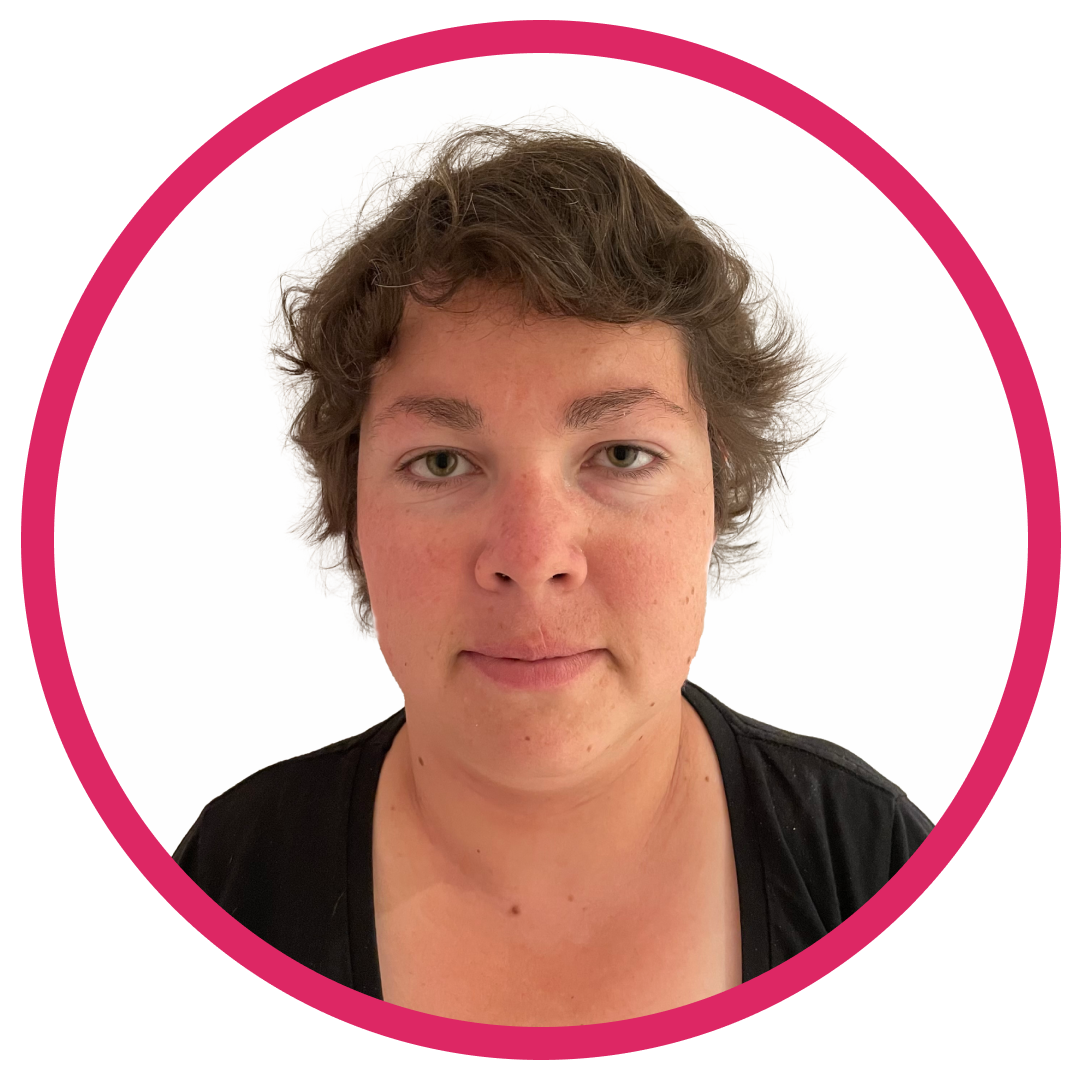 Portrait of Kyrby B, a woman with short, wavy brown hair, wearing a black top and facing directly at the camera smiling set inside a circular frame with a pink border.
