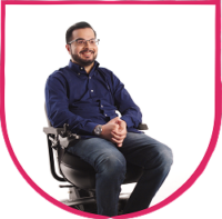 Fable Community member headshot 2 Man seated in a powered wheelchair, smiling with hands clasped